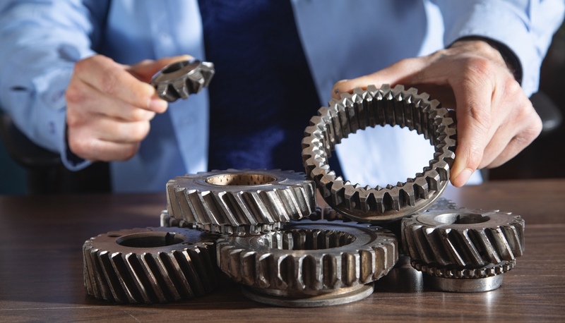 Man compares assorted metal gears, industrial gears, gear design