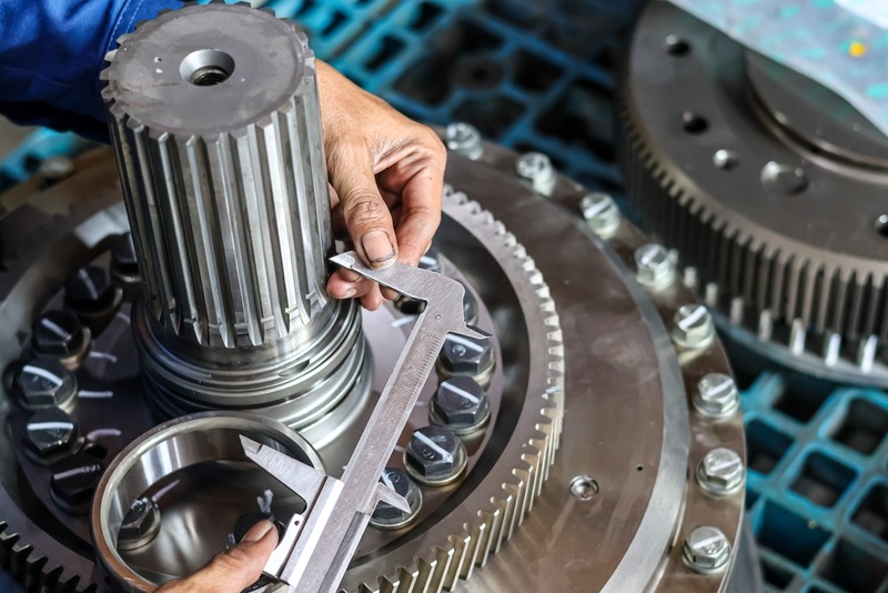 Technician measuring heavy duty metal spline shaft gear using vernier caliper tool in industrial workshop